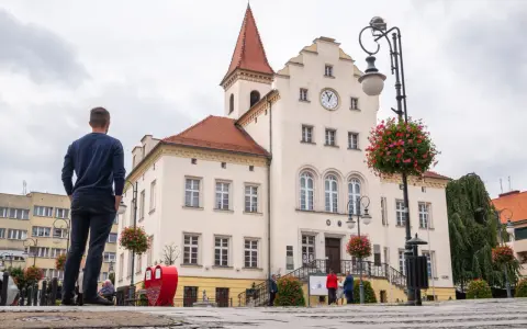 Mężczyzna podziwia ratusz w Trzebnicy, jedną z głównych atrakcji miasta. W tle czerwone serce i kwitnące kwiaty.
