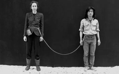 Une femme et un homme, reliés par une corde, dans une performance artistique saisissante.