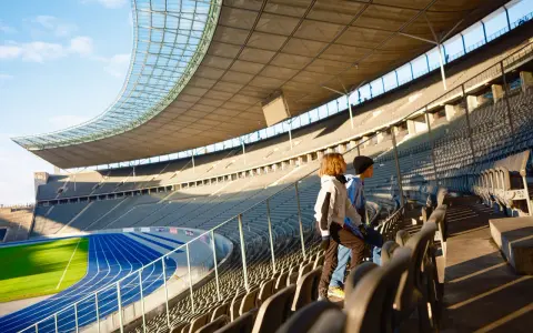 Zwei Kinder stehen auf den Rängen des Olympiastadion Berlin und blicken auf die Laufbahn.