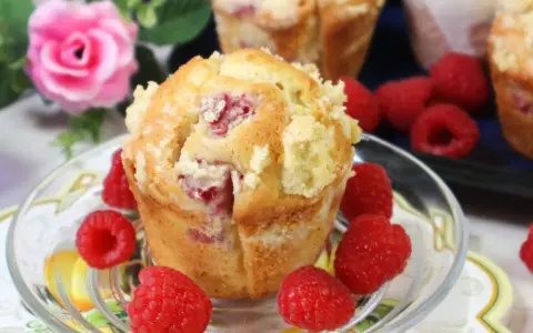 Pyszne muffinki z malinami, posypane kruszonką, otoczone świeżymi malinami.