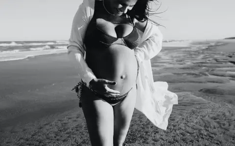 Donna incinta si gode il sole in spiaggia, accarezzando il pancione. La brezza marina le scompiglia i capelli.