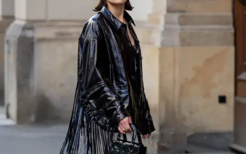 Mujer con vestido negro y chaqueta de charol con flecos. Un look audaz para combinar vestido negro con chaqueta.