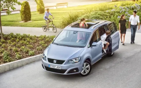 Familienauto mit zwei Kindern, die ein- und aussteigen. Ein Junge fährt Fahrrad im Hintergrund.
