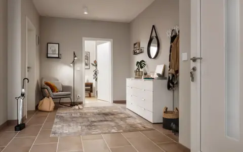 Stilvoller Flur gestalten: Grauer Sessel, Teppich, weiße Kommode mit Spiegel und Garderobe schaffen eine einladende Atmosphäre.