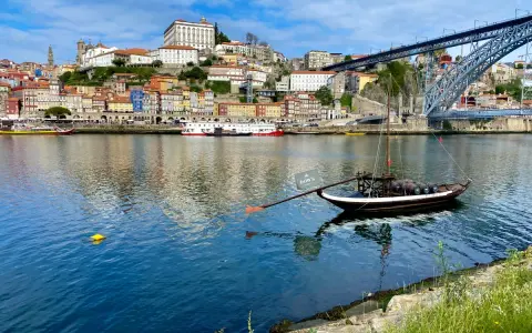 A traditional Rabelo boat with barrels, a symbol of Porto's wine heritage, floats on the Douro River. This iconic view is a must-see for any Porto travel guide.