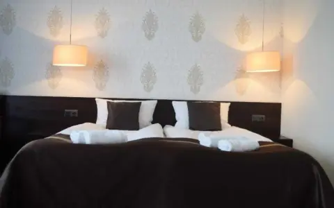 Przytulny pokój hotelowy z podwójnym łóżkiem, białymi ręcznikami i lampami. Czy można wynająć pokój w hotelu mając 17 lat?