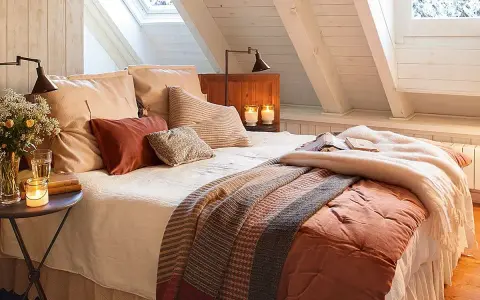 Dormitorios cálidos y acogedores bajo un techo abuhardillado. Cama con mantas de punto y cojines mullidos. Velas y flores crean un ambiente íntimo.
