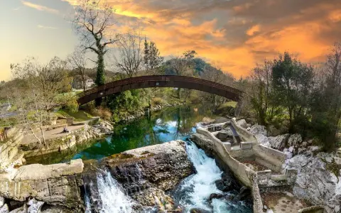 Un puente arqueado cruza un río verde, con cascadas y ruinas de piedra. Un paisaje idílico que invita a descubrir pueblos bonitos cerca de Puente Viesgo.