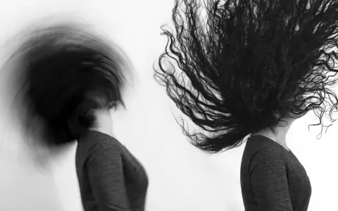 Dos cabezas con cabello largo y oscuro en movimiento, capturadas con un obturador fotográfico que crea un efecto de desenfoque dinámico.