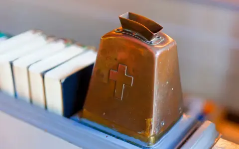 Kupferne Klingel mit Kreuz, bereit für Spenden. Hier wird über Kirchensteuer Befreiung nachgedacht.