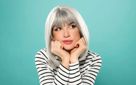 Donna con eleganti capelli grigi, appoggiata alle mani, con un'espressione sognante.
