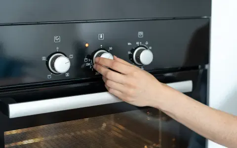 Hand dreht Temperaturregler am Ofen auf 250 Grad. Die Frage "wie lange Ofen vorheizen" wird durch das Einstellen der Temperatur beantwortet.