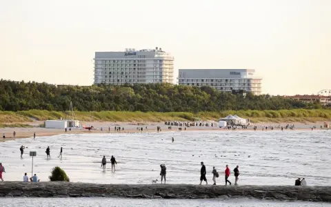 Ludzie spacerują po najszerszej plaży w Polsce, w tle hotele Radisson i Hilton.