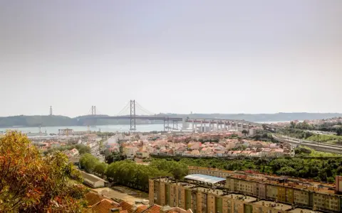 Blick auf Lissabon mit der Hängebrücke und dem Cristo Rei Denkmal. Im Vordergrund die Dächer von Häusern, die an den "Cemitério dos Prazeres" erinnern.