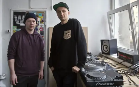 Dwóch mężczyzn przy sprzęcie DJ-skim. Jeden w bordowej bluzie z kapturem, drugi w czarnej bluzie z naszywką. To ich sposób na pokazanie, co to stereo.