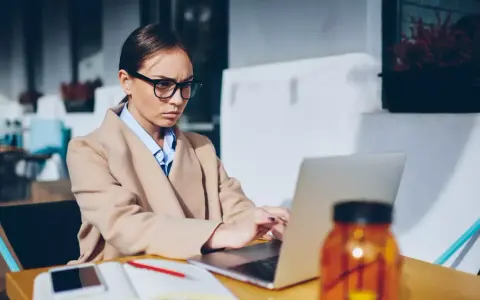 Donna con occhiali lavora al laptop, pensierosa sul gender pay gap in Italia.