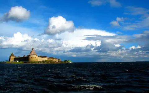 Forteca na wyspie nad największym jeziorem Europy, woda faluje pod błękitnym niebem z chmurami.
