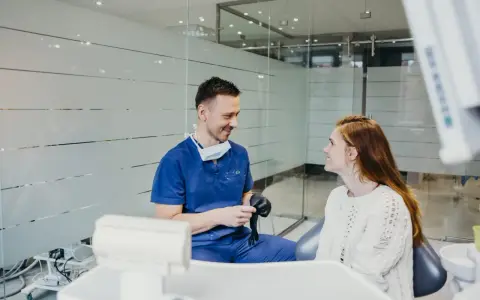 Dentysta w niebieskim uniformie rozmawia z pacjentką, sugerując nowy lek na ból zęba.