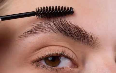 Une brosse à cils peigne les sourcils d'une femme pour les mettre en forme.