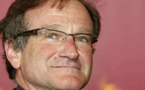 Primo piano di Robin Williams con occhiali, un uomo che ha portato gioia a molti, anche se il suo figlio morto non ha potuto vederlo.