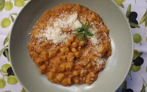 Pyszny makaron z ciecierzycy w sosie pomidorowym, posypany parmezanem i udekorowany gałązką rozmarynu.