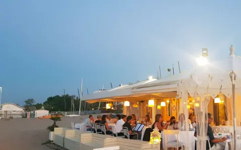 Serata in uno dei ristoranti della Riviera Romagnola, con tavoli apparecchiati sulla sabbia e luci soffuse.