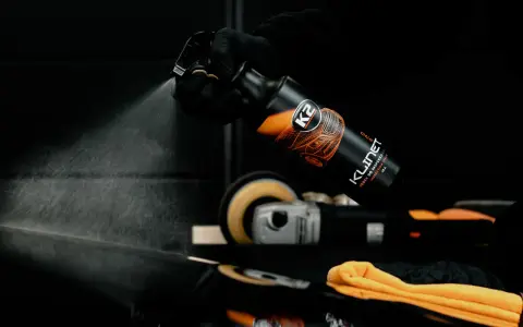 Rękawiczka w czarnej rękawiczce rozpyla produkt K2 KLINET na czarną powierzchnię, sprawdzając, czy aceton niszczy lakier samochodowy.