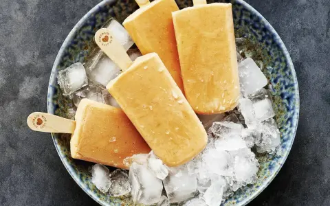 Vier selbstgemachte Papaya-Eis am Stiel liegen auf zerstoßenem Eis in einer blauen Schale.