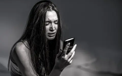 Ragazza piange guardando il telefono, vittima di revenge porn. La legge punisce chi diffonde immagini private senza consenso.