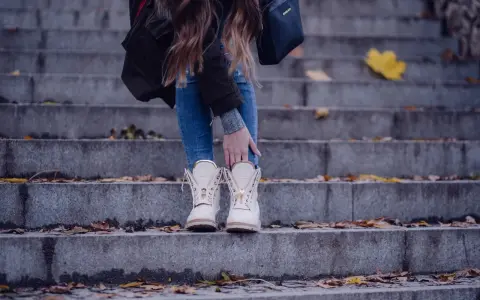 Kobieta w beżowych botkach na schodach, otoczona jesiennymi liśćmi.