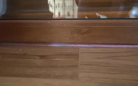 Drewniana listwa przy drzwiach balkonowych, z widoczną podłogą i fragmentem szyby.