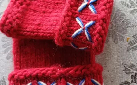 Närbild på röda, stickade vantar utan fingrar med korsstygn i vitt och blått. Perfekt för att virka vantar utan fingrar.