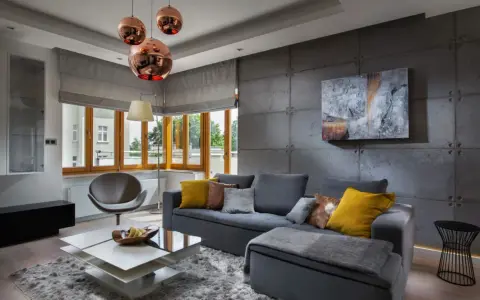 Nowoczesny salon z betonową ścianą. Inspiracje dla odważnych: szara sofa, miedziane lampy i geometryczne meble tworzą industrialny klimat.