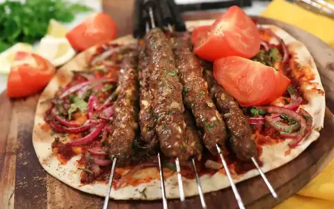 Grillade Adana kebabspett på en bädd av tunnbröd med rödlök, tomat och persilja. Ett perfekt adana kebab recept för en smakrik måltid.