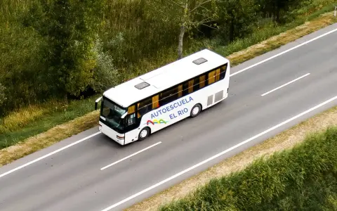 Autobús blanco de la autoescuela El Río en una carretera, preparándose para un examen en la pista.