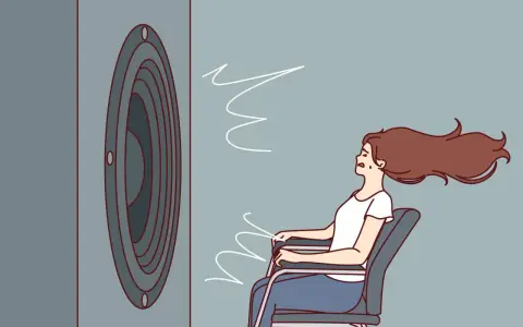 Une femme assise, les cheveux au vent, face à un haut-parleur. Le son est si fort qu'il en devient une force physique, illustrant la définition du décibel.