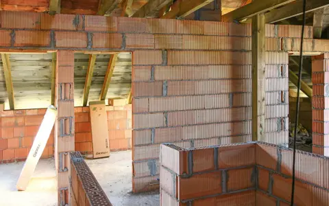 Budowa domu z pustaków ceramicznych. Widać niedokończone ściany, belki stropowe i materiały budowlane. Murowanie na piankę wady mogą pojawić się przy nieprawidłowym wykonaniu.