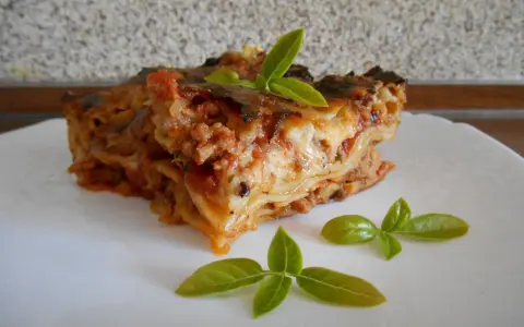 Kawałek pysznej lasagne z mięsem mielonym, udekorowany listkami bazylii. Prosty przepis na domową lasagne.