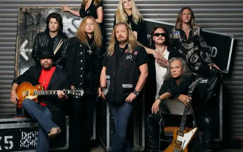 Medlemmar av Lynyrd Skynyrd poserar för ett gruppfoto. En man i förgrunden håller en gitarr.