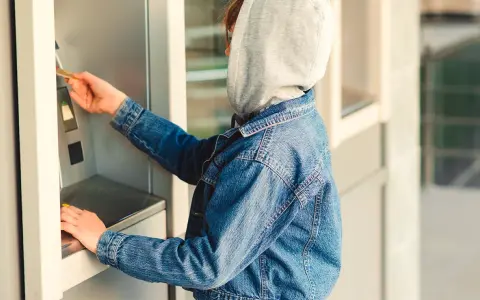 Jugendlicher mit Kapuze und Jeansjacke am Geldautomaten. Ein Beispiel für mögliche Verhaltensauffälligkeiten, die auf Kleptomanie bei Kindern hindeuten könnten.