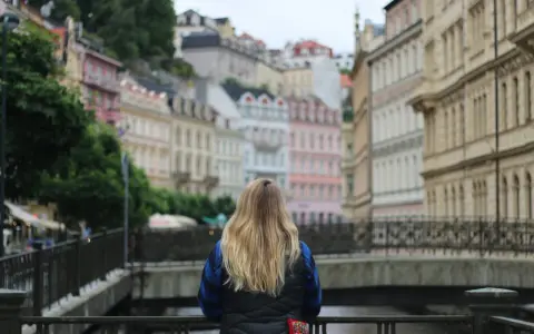 A woman with blonde hair gazes at colorful buildings, perhaps planning her day trips from Prague by train.