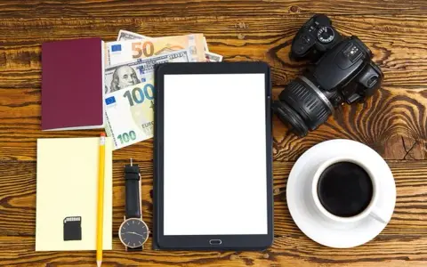 Planujesz podróż? Zastanawiasz się, ile kosztuje zdjęcie do dowodu u fotografa? Na zdjęciu paszport, pieniądze, aparat i tablet.