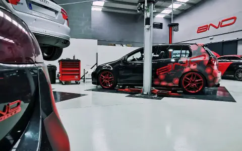 Taller con coches modificados. Uno negro con diseño de hexágonos rojos y llantas rojas, otro negro y rojo con alerón. Se pregunta cuánto cuesta reprogramar un coche.