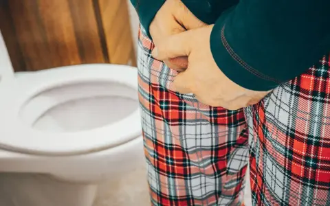 Osoba w piżamie z kratką przy toalecie, odczuwająca parcie na mocz przy cewniku.