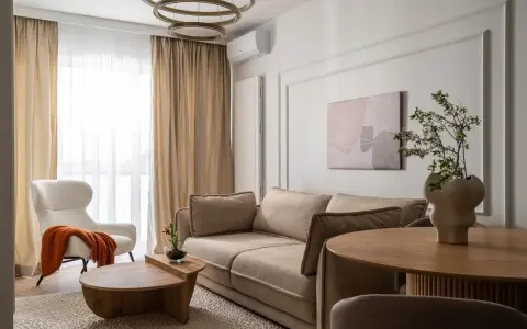 Nowoczesny salon szaro beżowy z wygodną kanapą, puszystym fotelem i drewnianymi meblami.