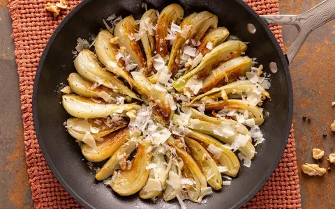 Finocchi in padella dorati e saporiti, guarniti con scaglie di formaggio e noci croccanti.