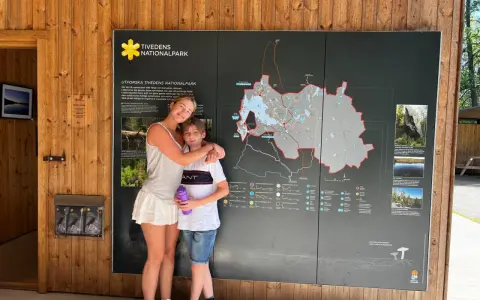 Två barn, en flicka och en pojke, står framför en karta över Tivedens nationalpark.