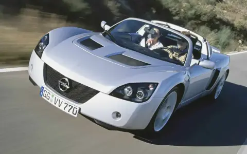 Srebrny Opel Speedster z dwoma pasażerami pędzi po krętej drodze.