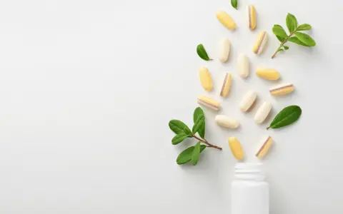 Kapsułki z lactobacillus plantarum rozsypują się z białej buteleczki, otoczone zielonymi listkami.