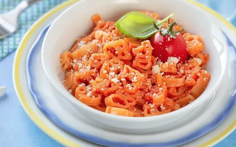 Makaron w kształcie zwierzątek z sosem pomidorowym, posypany parmezanem, udekorowany pomidorkiem i bazylią.